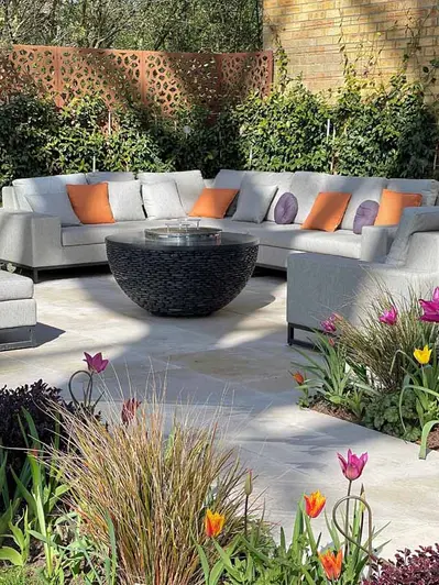 Corner of garden formed by wall and metal screen, with Jura Beige limestone patio paving, climbing plants and outdoor furniture.