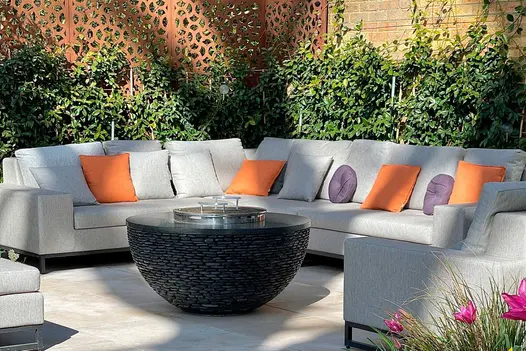 Jura Beige limestone contemporary paving in corner of garden with large modular sofa and chairs around covered fire pit.