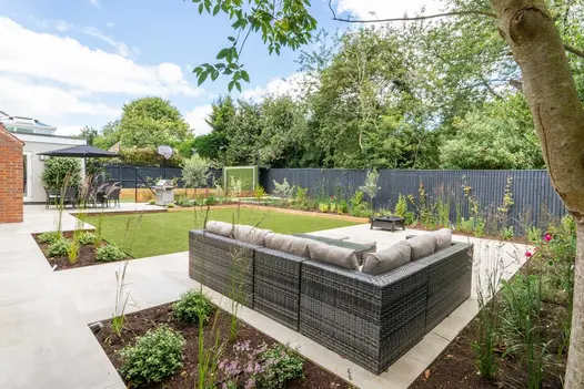 Rattan garden sofa on top of a Cream porcelain patio looking towards the house in a recently landscaped rear family garden.
