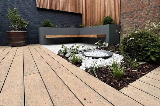 Porcelain paving flanks the warm teak brushed composite decking, featuring a floating bench and surrounding plants.