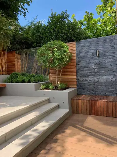 Black Slate Cladding used as feature wall inbetween fence panels, steps lead up to patio from decking area.