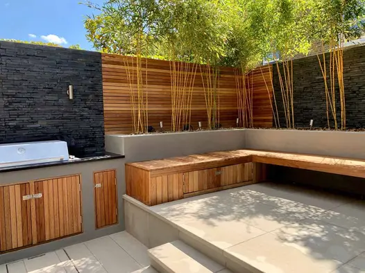 BBQ area uses black slate cladding as backsplash, raised flowerbeds host a floating bench to the right.