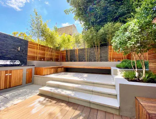 Two steps lead up to small patio with floating bench surrounded by fencing clad with wood and black slate cladding.