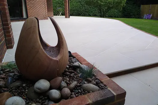 Florence Beige porcelain patio at back of house, paving slabs laid at angle by Transform Landscape Services. Water feature by step.