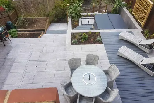Terraced back garden stepping down and away from the house featuring a paved dining area, sun loungers and a hot tub.