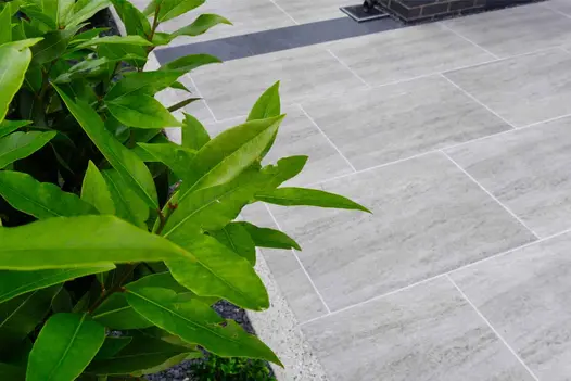 600x600 sized Dark Travertine porcelain paving slabs grouted with white grout and a gravel planted border feature.