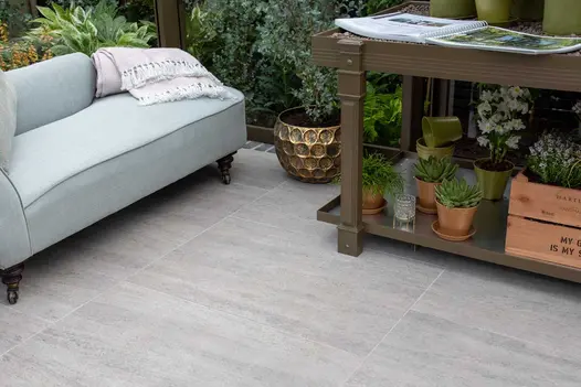 Staged photograph of an outdoor living room with sofa, plant trolley storage and a Travertine Dark porcelain patio.