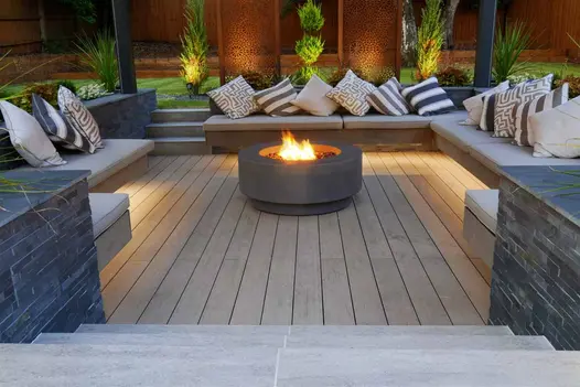 Set of Travertine Dark Porcelain steps leading down towards a sunken firepit surrounded by floating benches and composite decking.