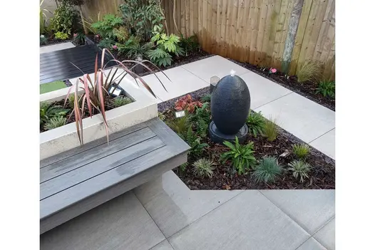 Trendy Black Porcelain paving cut at angle to edge trapezium-shaped planted bed with water feature. Design by Floral & Hardy.