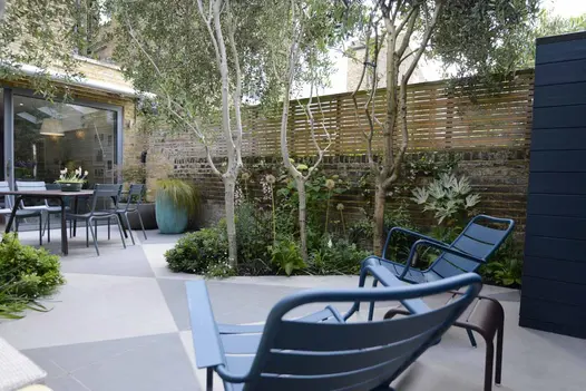 Stylish courtyard garden design, utilizing trendy black and urban grey porcelain in angular cuts, surrounded by fencing and trees for privacy.