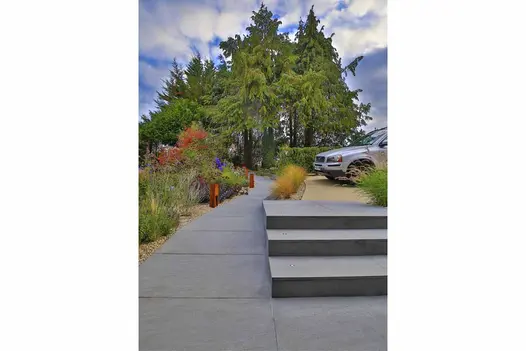 Three Trendy Black porcelain steps, lights set into each tread, rise from path between borders to hard standing with car.