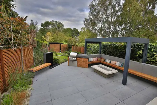 Patio in Trendy Black Porcelain. Pergola over fire-table and benches cantilevered into wall faced in matching porcelain tiles.