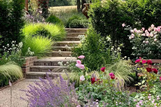 Pebble path leads to 9 Tumbled Black Sandstone Rock-Faced Step with vibrant and bursting plants on either side.