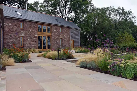 Modern barn construction fronted with large area of Tumbled Raj Green sandstone paving with rectangular beds inset.