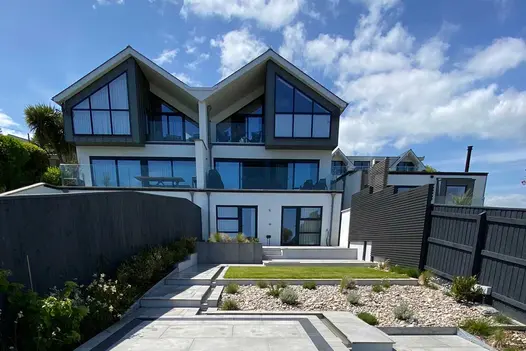 Long garden of modern 3-storey semi-detached house is partially bordered by stepped screening of Dark Ash composite battens.