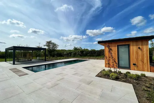 Stunning garden view using Urban Grey Porcelain showing blue skies with clouds, impressive pergola stands in the background behind an inviting pool.