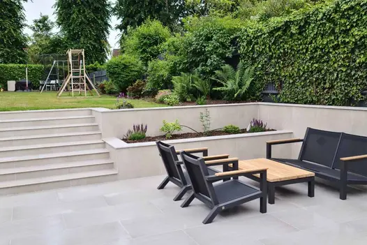 Patio area paved with Urban Grey vitrified porcelain paving, featuring modern metal garden furniture set with a wooden top.