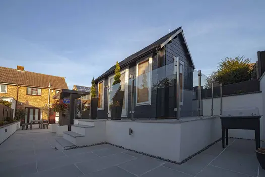 4 steps rise to garden room on plinth at end of long garden completely paved in Urban Grey porcelain designed by AG gardening.