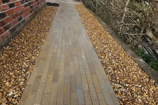 Antique Yellow Stone Pavers create a pathway down an alleyway, flanked by pebbles on both sides, leading to another part of the garden.