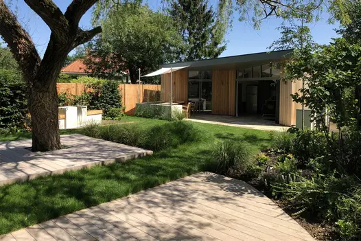 2 composite decking areas of Cinnamon DesignBoard, 1 with tree in centre, , set into lawn next to garden building. Design by VaRa.