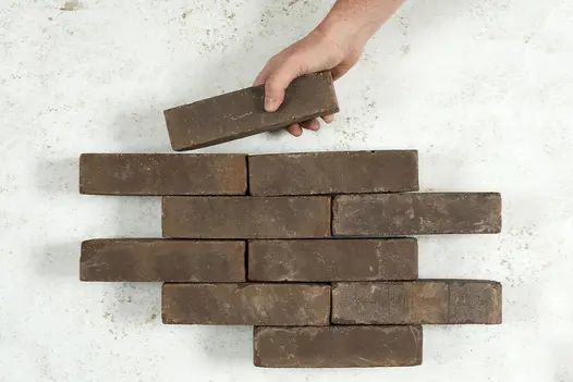 A hand places a Verona Clay Paver into a formation of nine bricks arranged in rows of one and two. Free UK delivery available.
