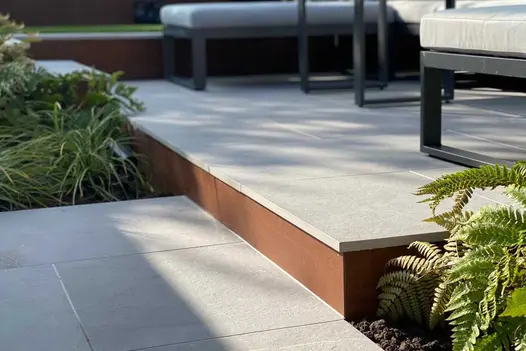 Multi level patio using porcelain for paving, shows vintage steel premium designclad used as step fascias.