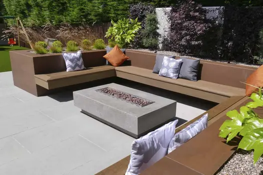 Firepit sits in the middle of a floating bench sat on patio, raised walls surround clad with vintage steel premium designclad.