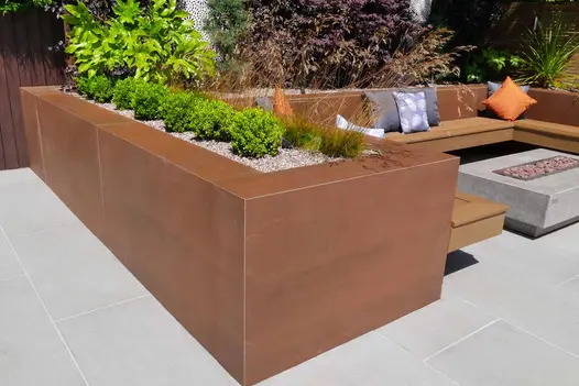 Corner view of raised planter clad in vintage steel premium designclad surrounding a floating bench and firepit.