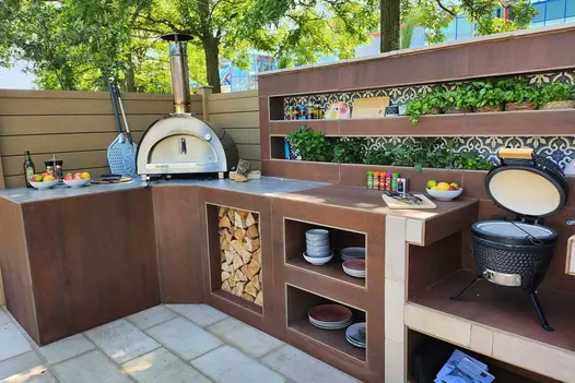 Outdoor cooking area clad in vintage steel premium designclad shows pizza over, crepe maker and log storage.