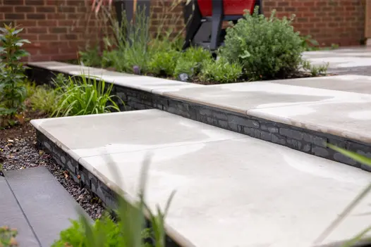 Light-coloured bullnosed steps have black slate cladding on the underside with inset flowerbeds either side.