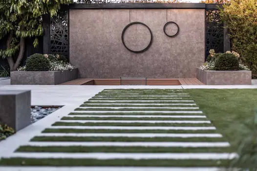 Low level view of feature wall clad with vulcano ceniza designclad sees light paving interspersed with lawn, creating plank effect.