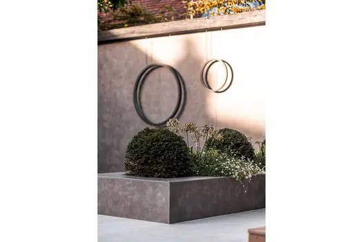 Feature wall sees 2 rings hanging in the distance, rasied flowerbed clad in vulcano ceniza porcelain cladding with topiary bushes.