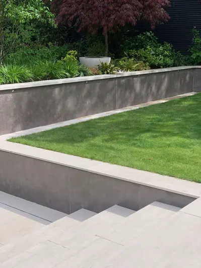 Steps descend from level of lawn to path next to retaining wall faced with Vulcano Ceniza luxury DesignClad wall cladding. 