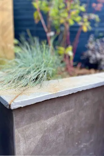 Close up view of Vulcano Ceniza Luxury DesignClad used on built in flowerbeds, planting seen out of focus in the background.