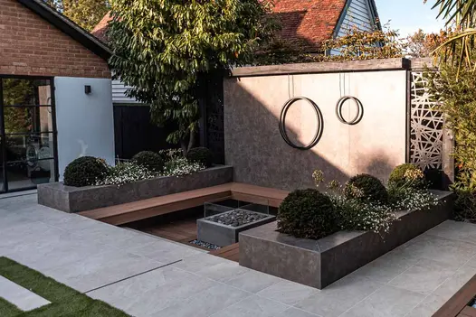 Sunken seating area with firepit has large wall and raised flowerbeds clad with vulcano ceniza designclad.