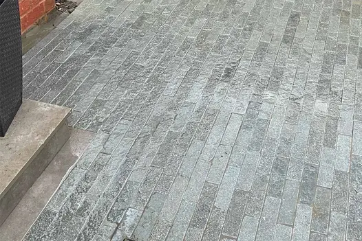 A gleaming surface of wet Antique Grey stone pavers unveils their silky texture, built by Paved In Stone.