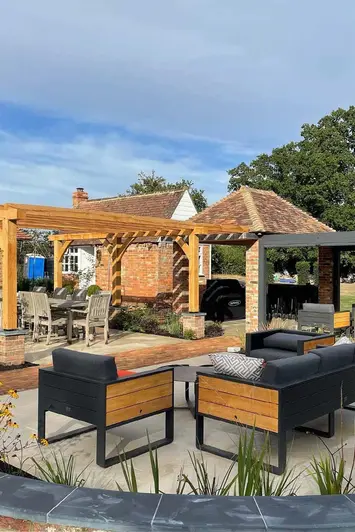 Blue skies fall on large garden with 2 pergolas and numerous seating areas, red brick house in the background.