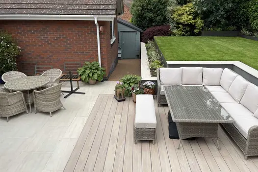 Aerial view of elevated lawn area that leads down to cinnamon designboard composite decking space with corner rattan couch and glass table.