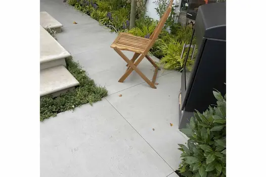 Garden path laid in Yard 1200x1200 porcelain adjacent to a set of natural stone steps with a log burner and wooden chair.