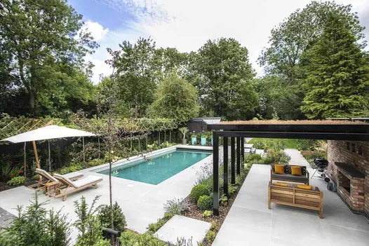 Large garden surrounded by trees, paved in Yard Outdoor Porcelain Paving, with pergola, swimming pool and garden furniture.