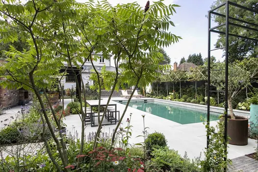 Steps descend from house to swimming pool edged in Yard Porcelain Pencil Round Coping and matching paving with inset flower beds.