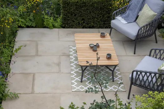 View down onto small patio of Britannia Buff sawn York stone with coffee table on outdoor rug and 2 chairs.